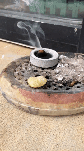 An animated GIF of a chunk of frankincense smoking on top of a charcoal disk.
